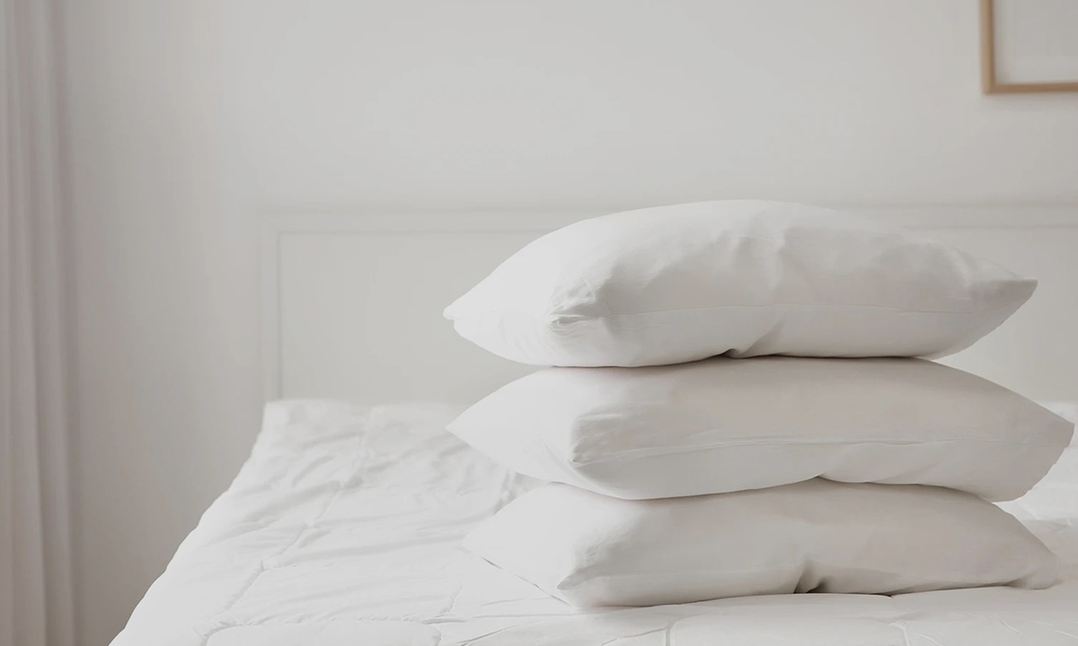 A bed with white sheets and three white Giselle Bedding pillows.