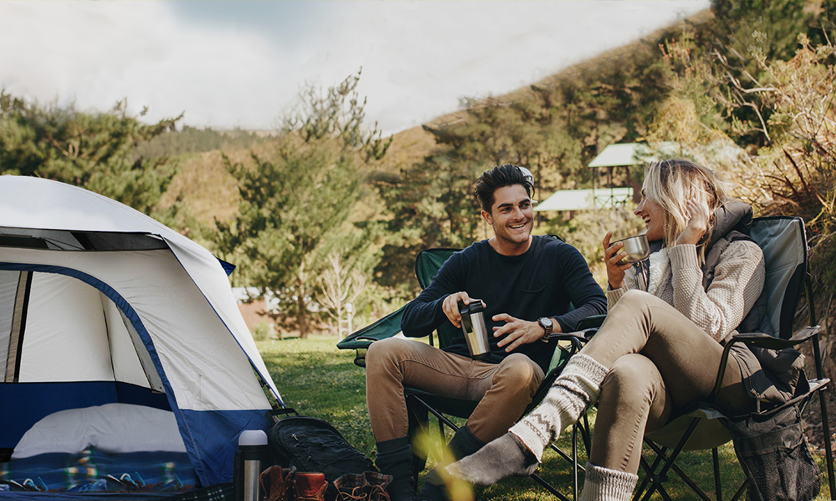 A couple laughing, sitting on Weisshorn camping chairs outside a tent.